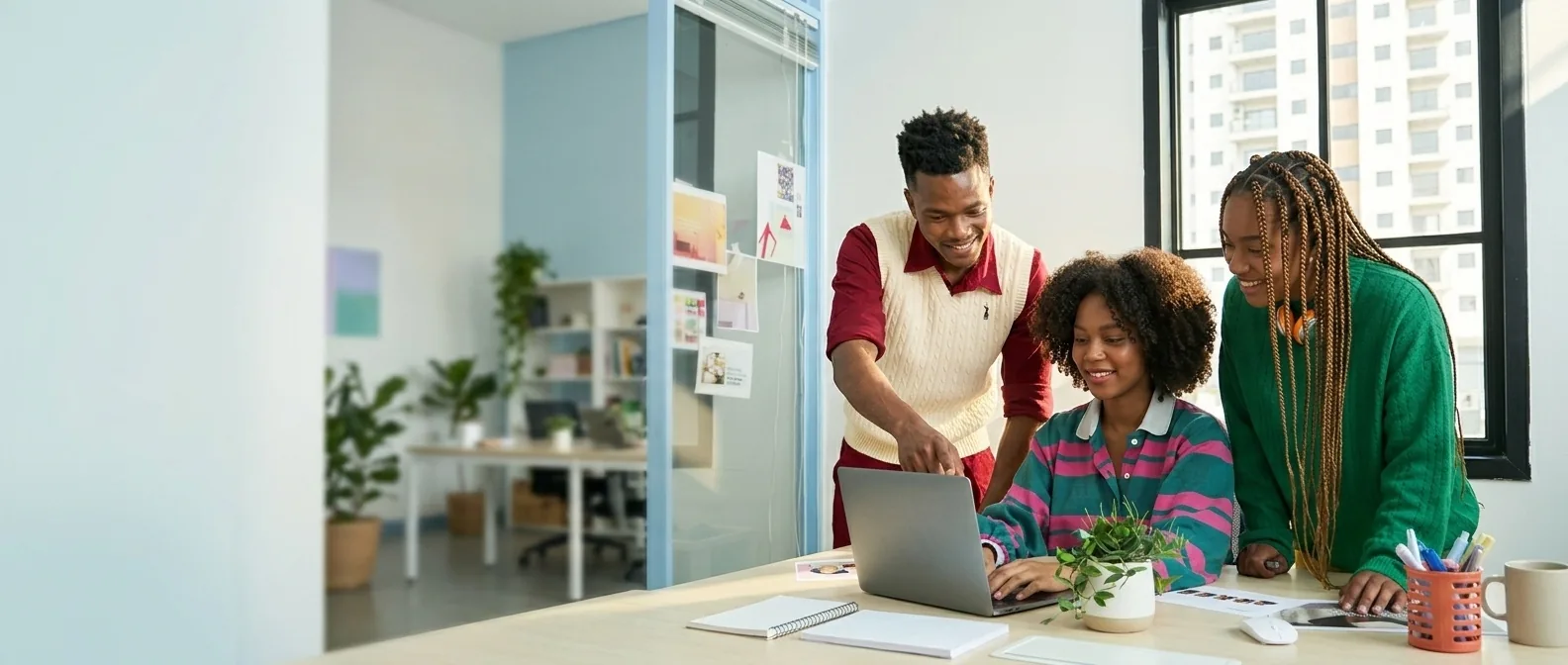 Three colleagues around a laptop in a bright office, smiling as they look at the screen together